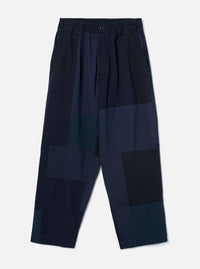 The Navy Patchwork Twill Oxford Pant is laid flat against a light grey backdrop. Features a wide-leg fit, elasticated waistband with single button, slant side pockets, and irregular patchwork panels in shades of navy, teal, and black twill.