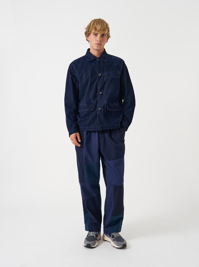 Full-length front view of a model wearing the Navy Patchwork Twill Oxford Pant in a studio setting with a plain white background, highlighting the relaxed fit, pleated front, and navy cotton fabric.
