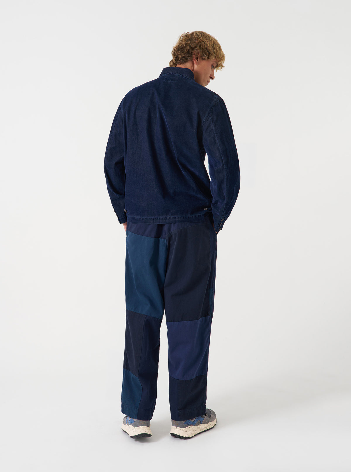 Back view of a model wearing the Navy Patchwork Twill Oxford Pant against a clean studio background, showcasing the relaxed tailoring, waistband, and textured navy patchwork twill material.