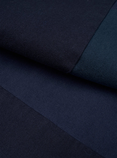 Close-up detail shot of navy twill fabric from the Oxford pant, showing the diagonal weave texture. Two contrasting panels of navy and dark teal twill meet at a sharp seam, highlighting the patchwork construction. No model or mannequin present.