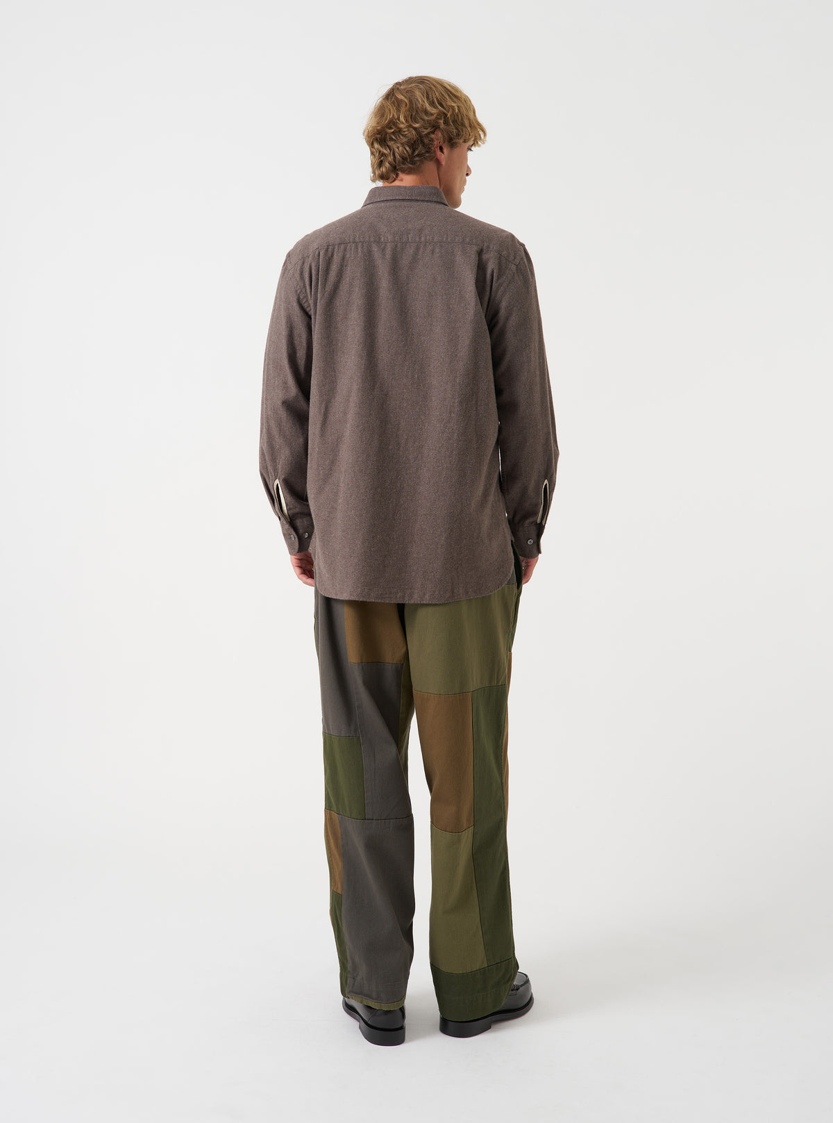Back view of a model wearing the Olive Patchwork Twill Oxford Pant against a plain backdrop, featuring the relaxed cut, drawstring waistband details, and olive green patchwork fabric structure.