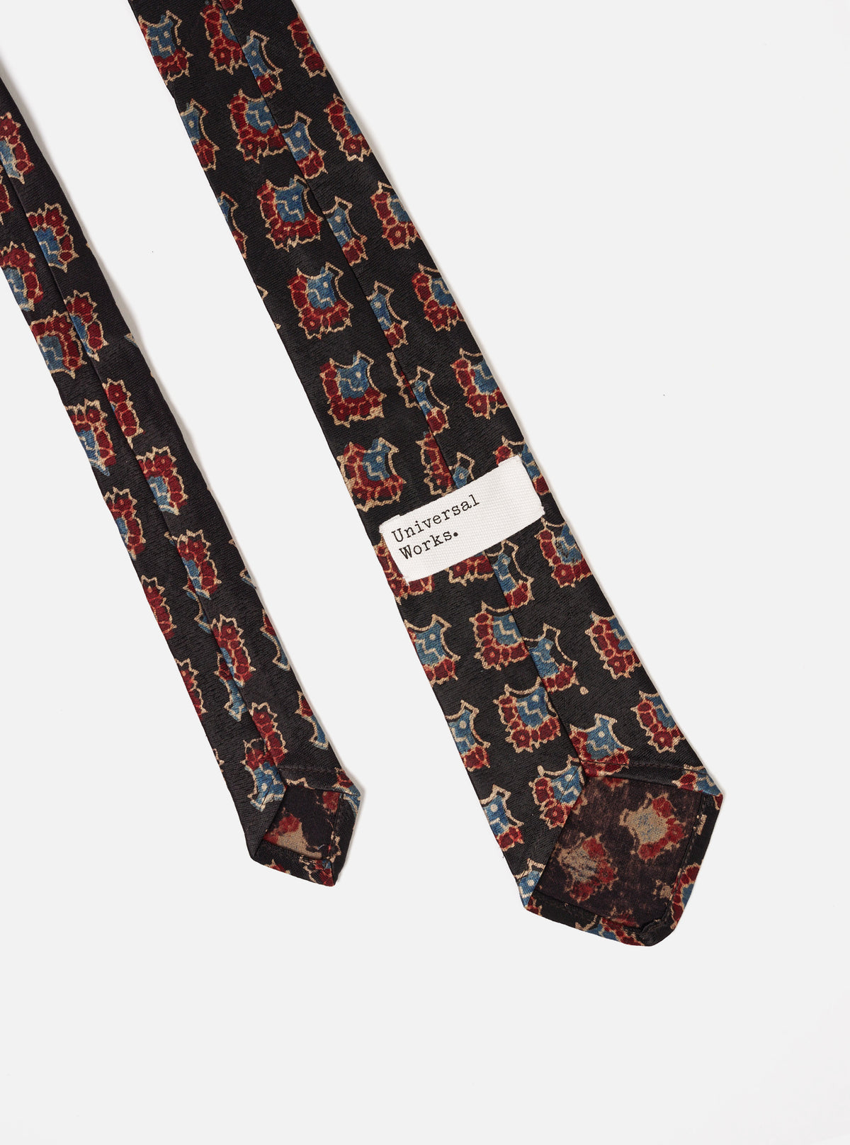 Angled product shot of the Black Mini Kalamkari Print Tie laid flat on a neutral background, highlighting the tail tip construction, precise stitching, and elegant black printed design.