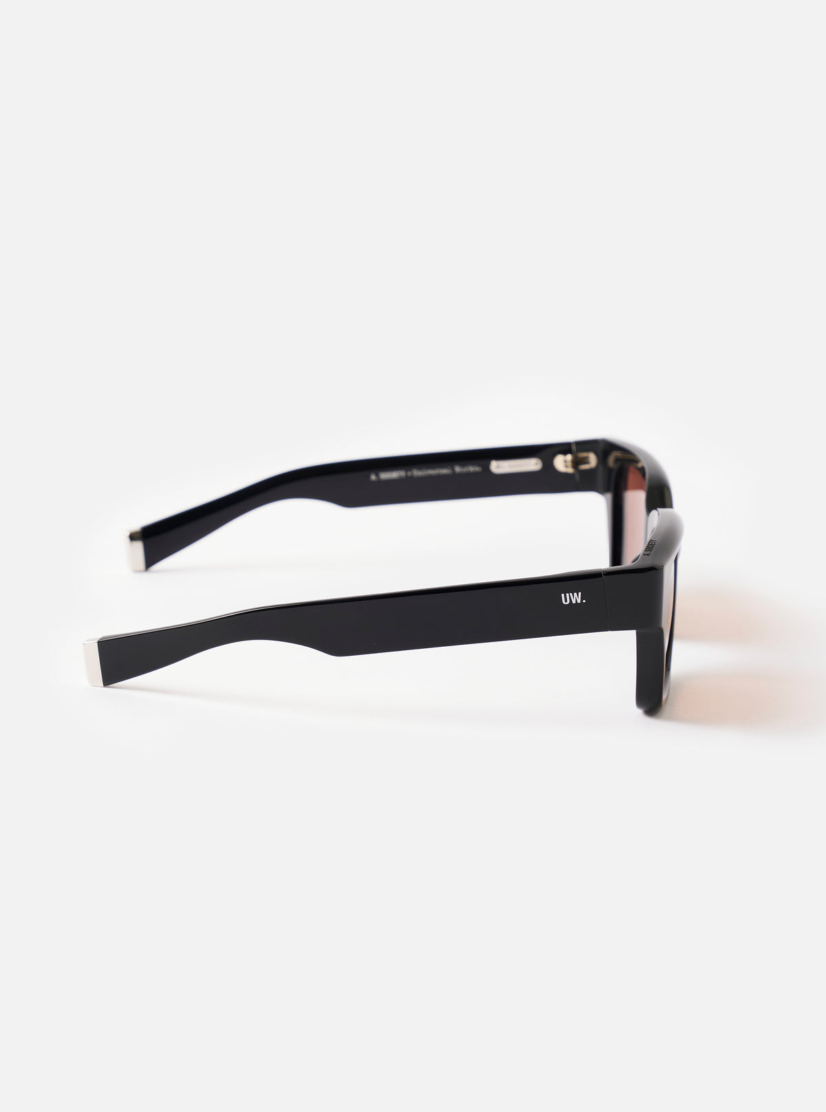 Three-quarter angled view of the A. SOCIETY x Universal Works Black Hollywood Sunglasses against a plain backdrop, highlighting the sculpted bridge and dark lenses of the classic frame.