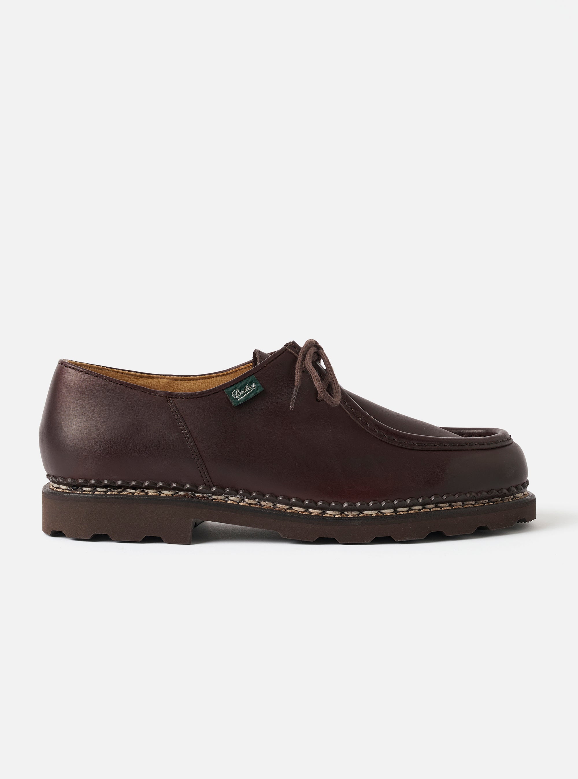 Paraboot Michael Marche II in cafe brown smooth leather, shot in profile against a plain light grey studio backdrop. Moc-toe construction with visible hand-stitched seam, two-eyelet lace-up fastening with brown waxed laces, and a small green Paraboot branded tongue tag. Chunky dark brown lugged rubber sole with contrast welt stitching.