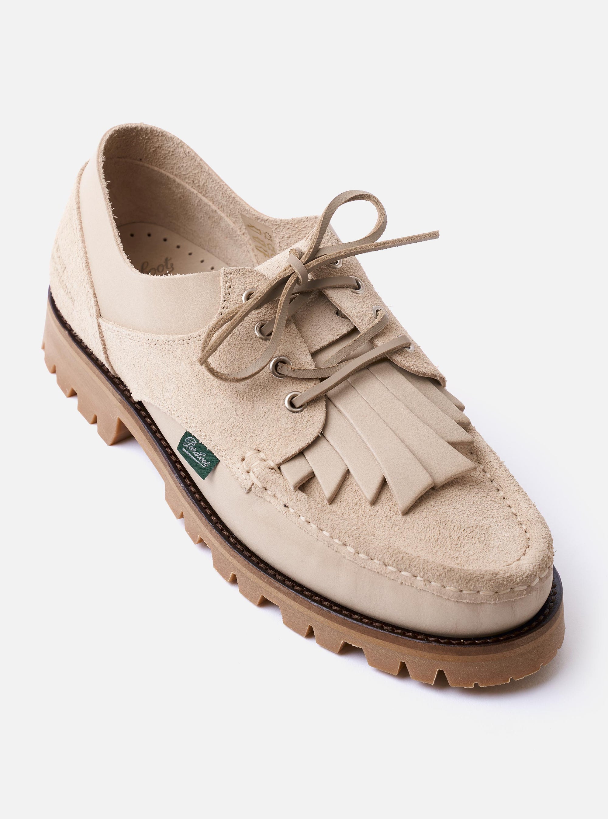 The Paraboot x Universal Works Thiers/Jannu in Sand Leather/Suede is shown from a rear three-quarter angle as a flat lay against a plain white background. The image highlights the light beige sand color, the contrast between the smooth leather and textured suede-like reverse panels, and the vulcanised natural rubber sole. The piped seams and Blake stitch construction are visible.