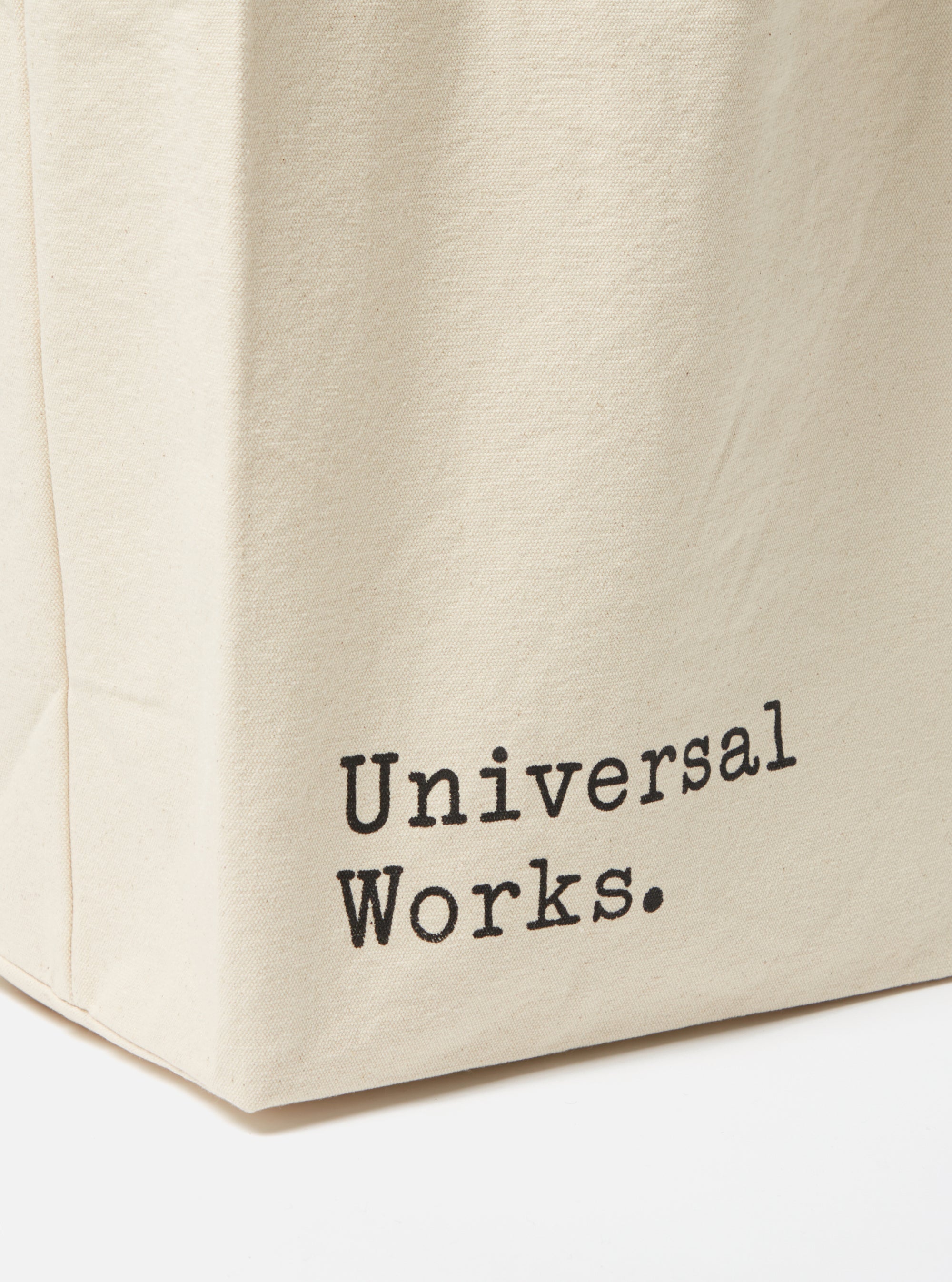 Close-up of an Ecru Cotton Canvas Tote Bag on a white surface. The bag has 'Universal Works.' printed on it in black.