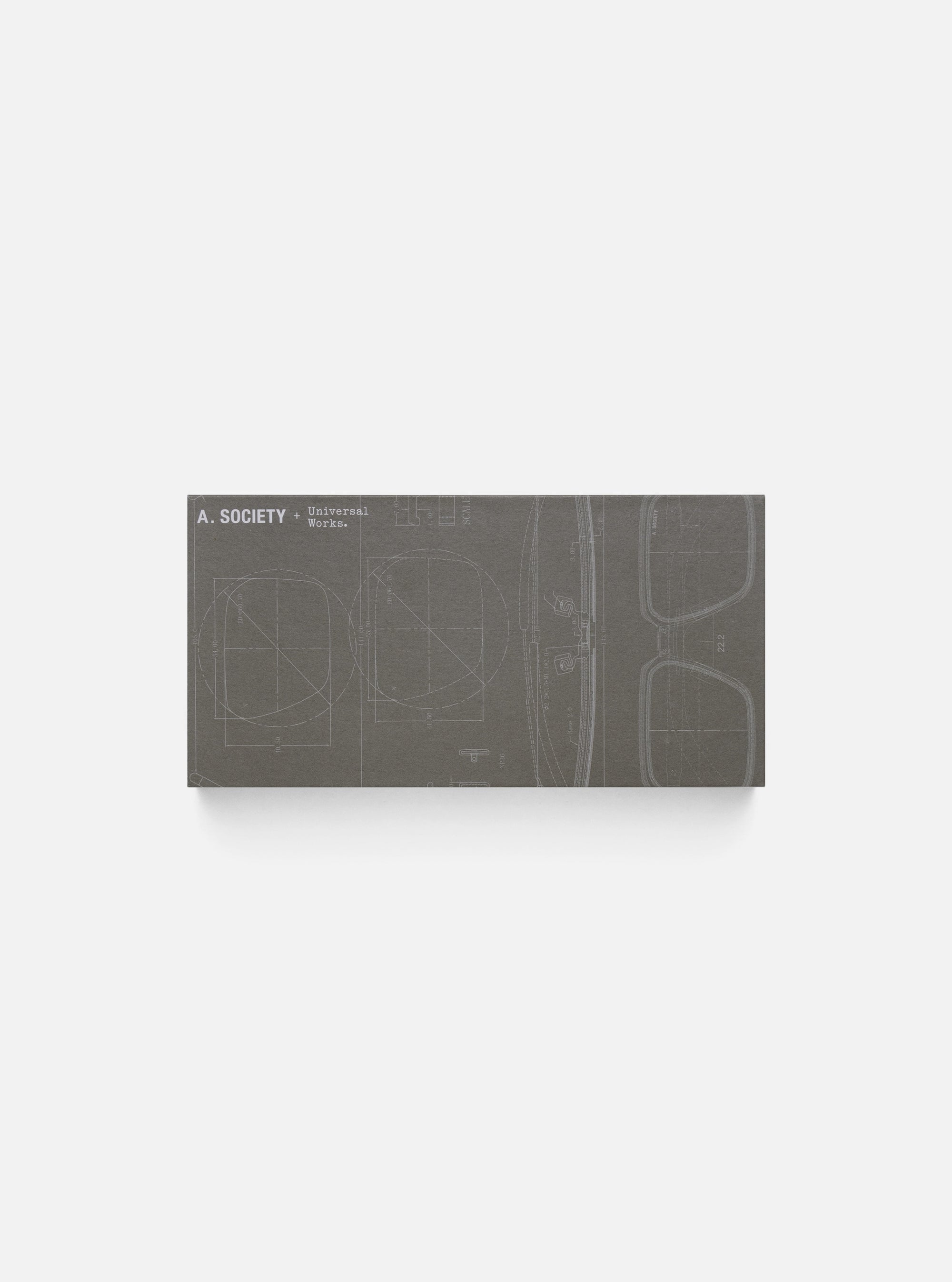 Close-up of the A. SOCIETY x Universal Works Green Aberdeen Sunglasses box on a white surface. The box has a blueprint design of the sunglasses.