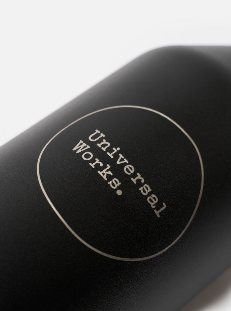 Studio product photograph showing the Chilly's x Universal Works Onyx Series 3 500ml Water Bottle positioned on a white surface, highlighting its carry loop lid and sleek bottle shape.