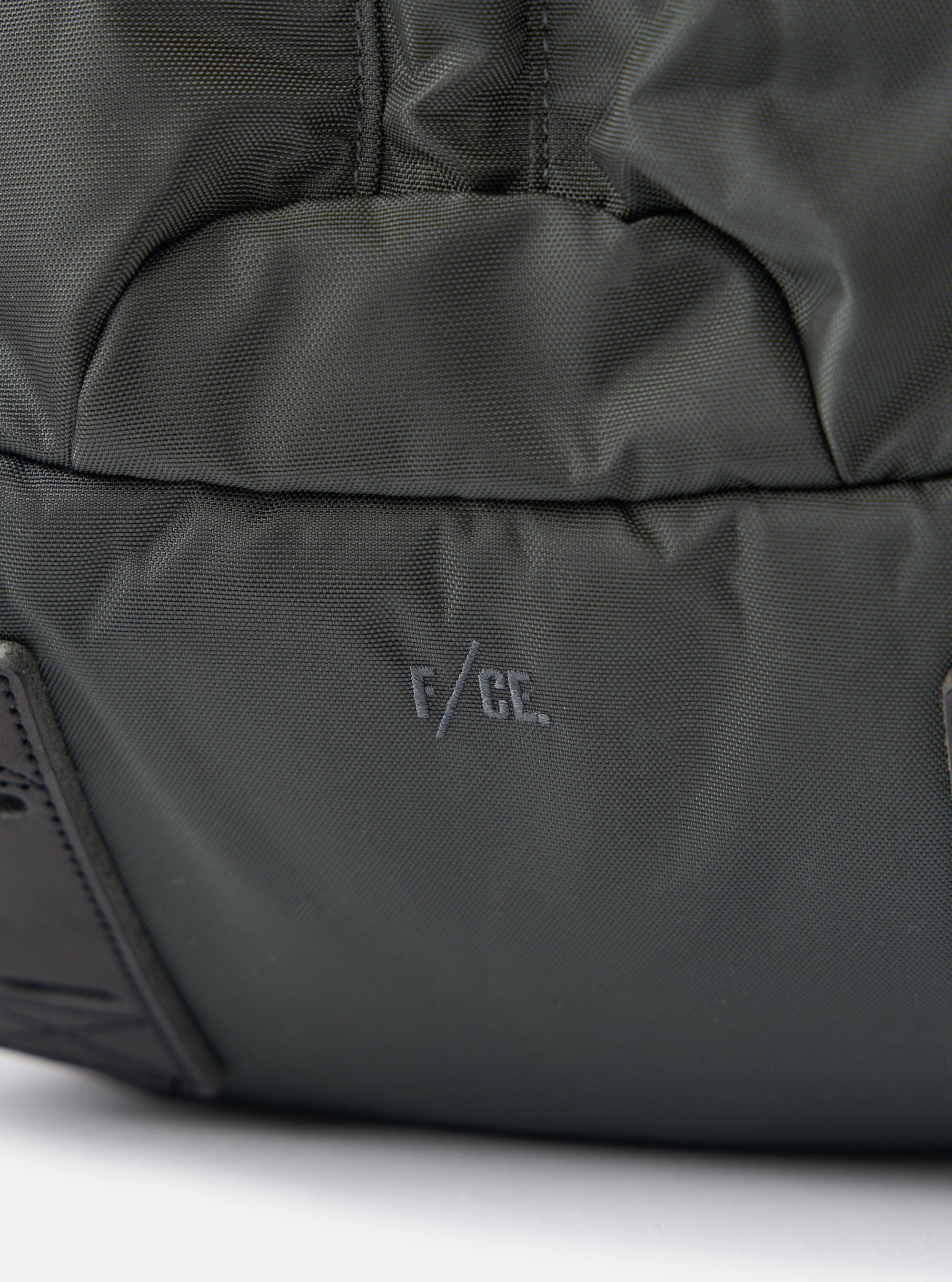 Close-up of the F/CE.® Grey Recycled Nylon 420 re/cor Travel Backpack on a white surface. The brand logo is visible on the grey nylon material.