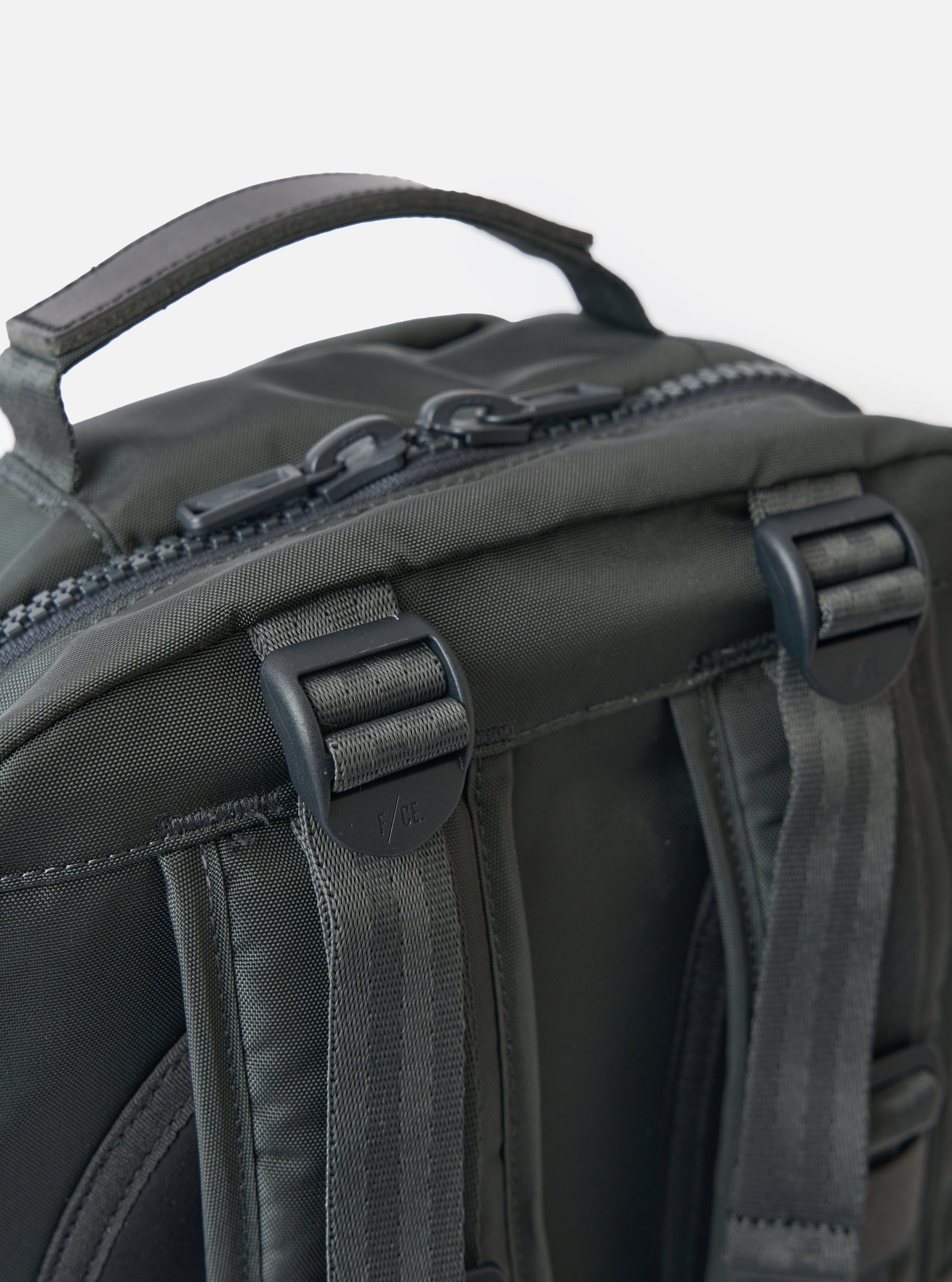 Close-up of the F/CE.® Grey Recycled Nylon 420 re/cor Travel Backpack. Shows grey nylon material, black zippers and straps. Shot against a white background.