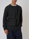 A model showcases the F/CE.® Black 420 re/cor Sacoche against a plain backdrop. The black bag is worn across the body with a dark sweater and blue pants.