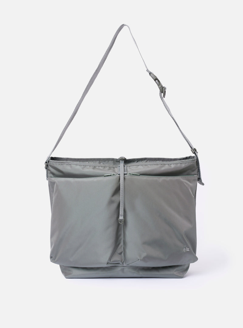 The F/CE.® Foliage Green Recycled Nylon 420 re/cor Courier Shoulder Bag is displayed as a flat lay against a plain white background. The bag features two large, prominent front pockets with top flaps and a wide, adjustable shoulder strap. The foliage green recycled nylon fabric has a technical, durable finish.