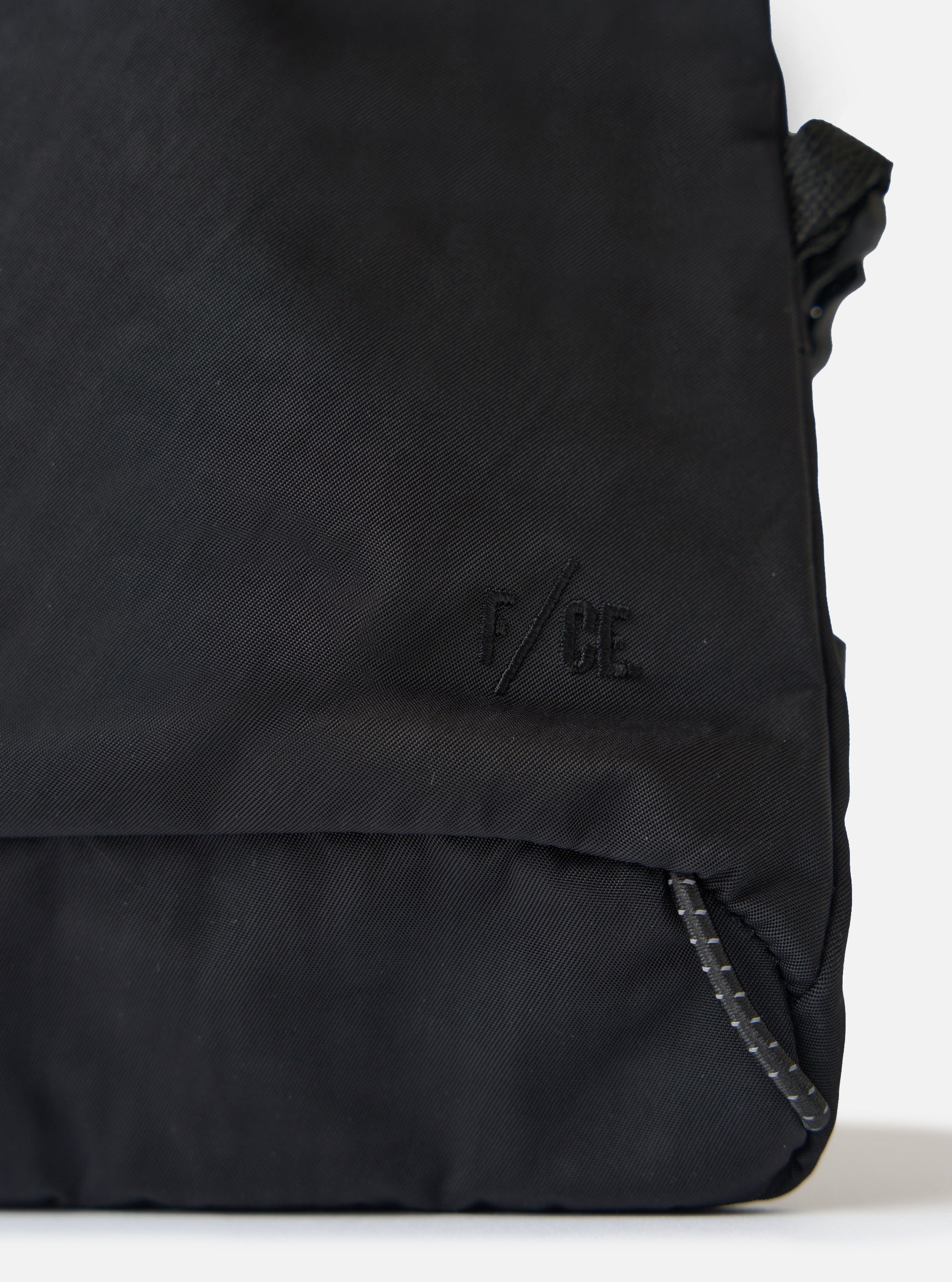 Close-up of the F/CE.® Black Nylon Textured Twill Drawstring Sacoche on a white surface. Shows the textured nylon, drawstring detail, and subtle branding.