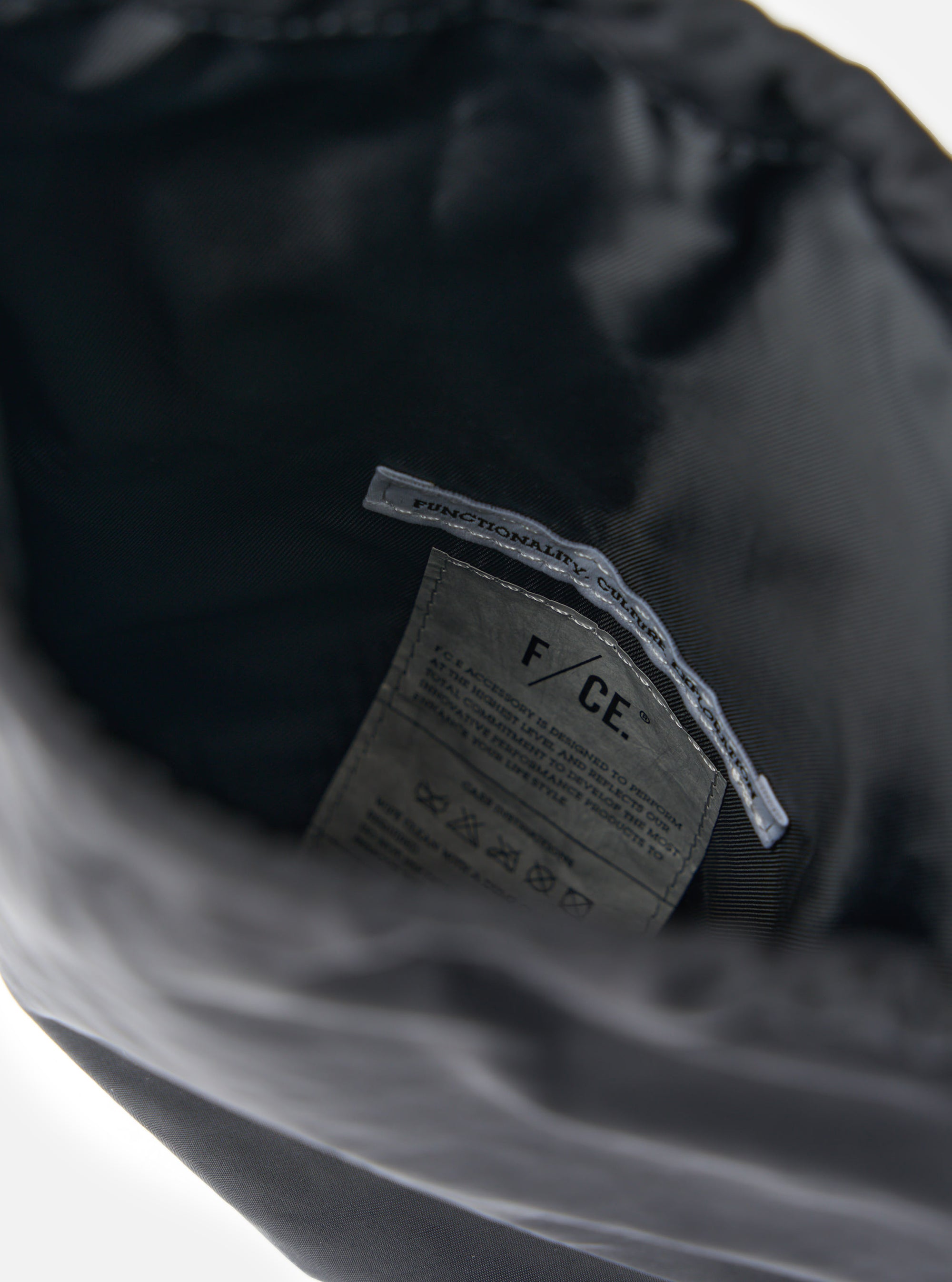 Close-up of the inside of the F/CE.® Black Nylon Textured Twill Drawstring Sacoche, showing the material and brand label on a white background.
