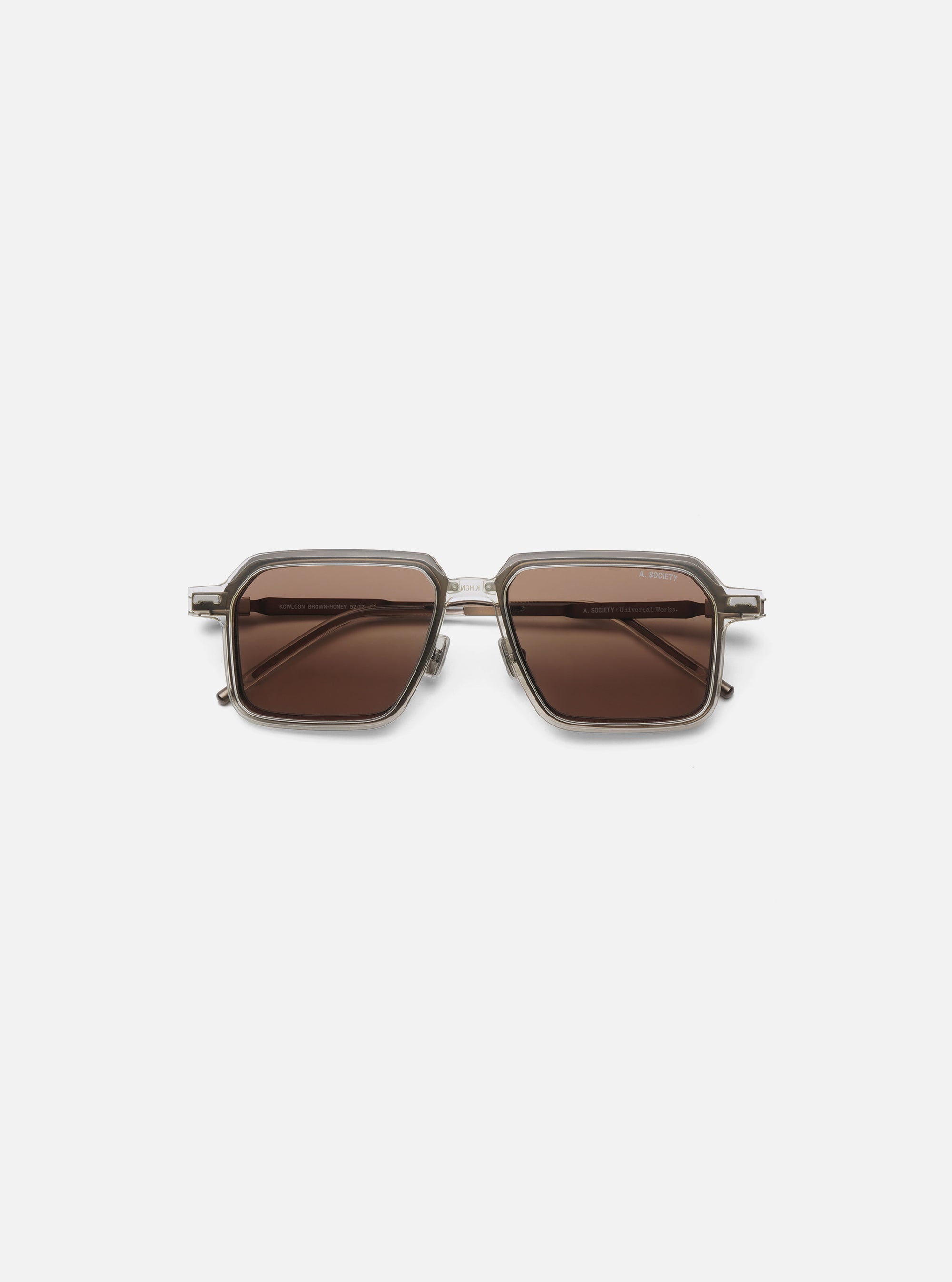 A. SOCIETY x Universal Works Kowloon Eyewear in brown and honey tones. Square frames with honey-colored lenses. Shot on a clean, white background.