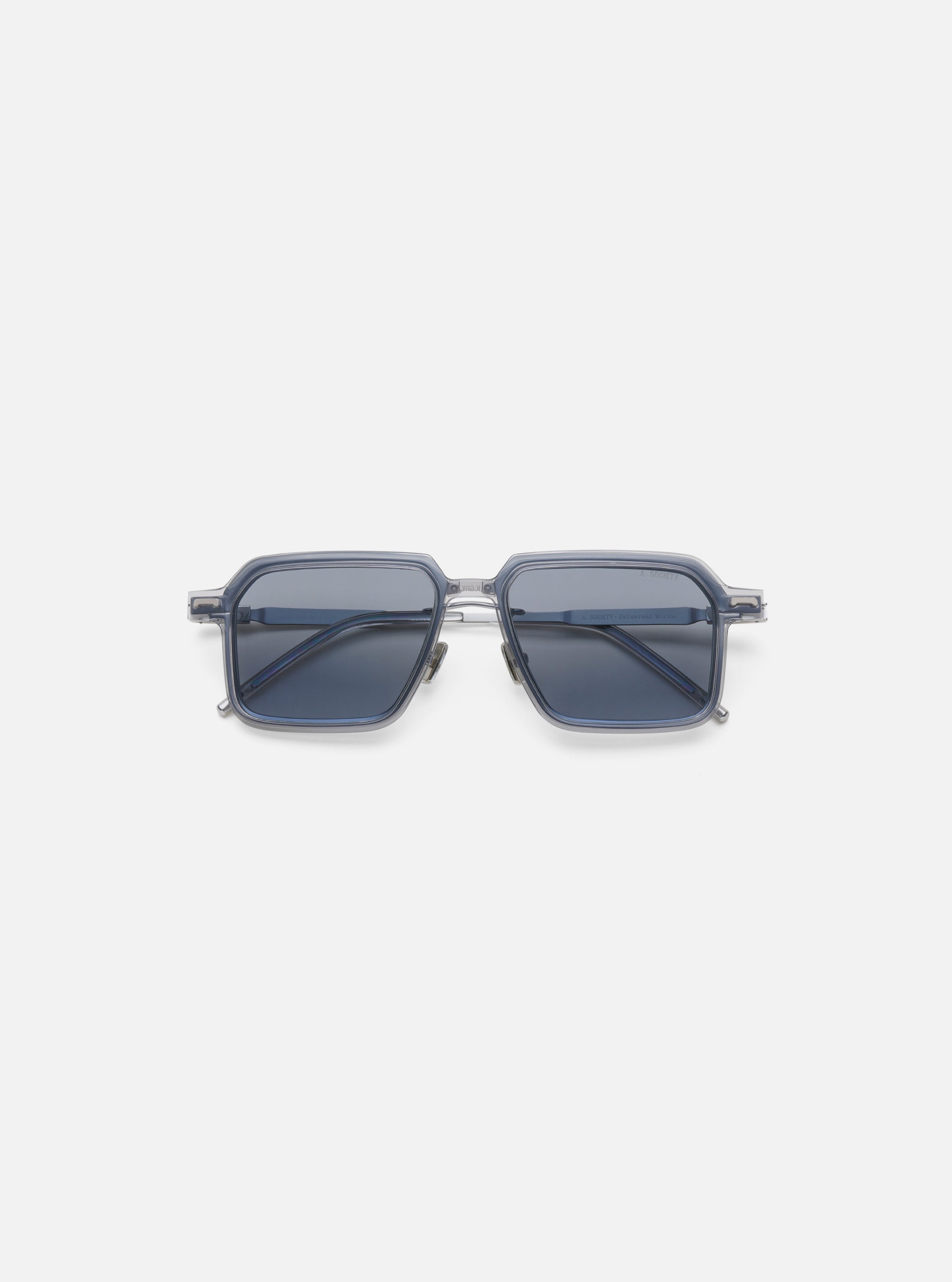 A. SOCIETY x Universal Works Silver/Grey Kowloon Eyewear on a white background. These square framed glasses have silver metal details and grey tinted lenses.