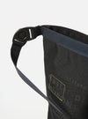 Close-up of the master-piece x Universal Works Black Recycled Tech Canvas Large Tote Bag. The black canvas material is visible with gold accents. Shot against a white background.