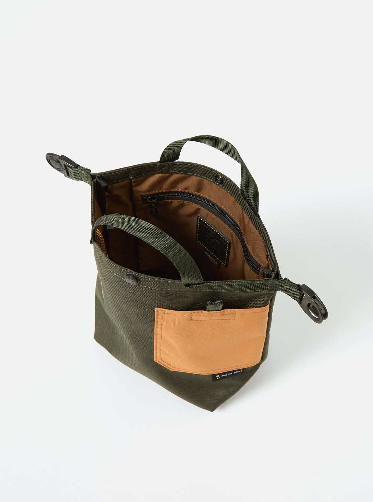 Olive master-piece x Universal Works small tote bag in recycled tech canvas. Features a tan pocket, olive straps, and brown interior. Shot on a white background.