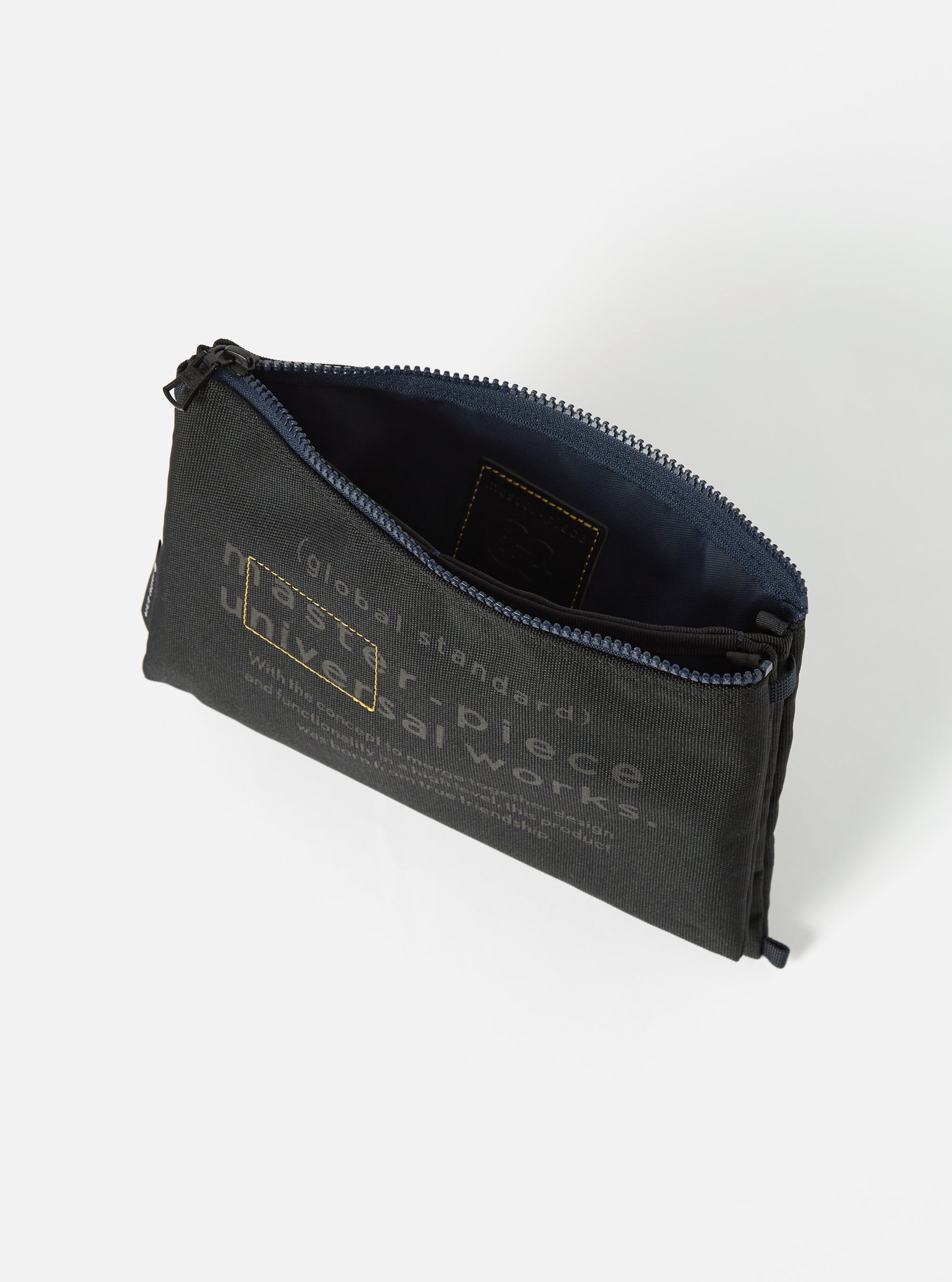 Close-up of the master-piece x Universal Works Black Recycled Tech Canvas Sacoche, showcasing its black tech canvas material and open zipper, staged on a white background.