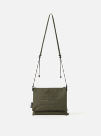 master-piece x Universal Works Olive Recycled Tech Canvas Sacoche on a clean white background. The olive green bag features black drawstrings and subtle branding.