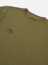 The master-piece x Universal Works Olive Single Jersey Print Tee is shown as a flat lay against a white background. The image displays the back of the olive green t-shirt, featuring a large graphic print of a geometric mountain landscape in orange and black. The garment has short sleeves and a ribbed crew neck.