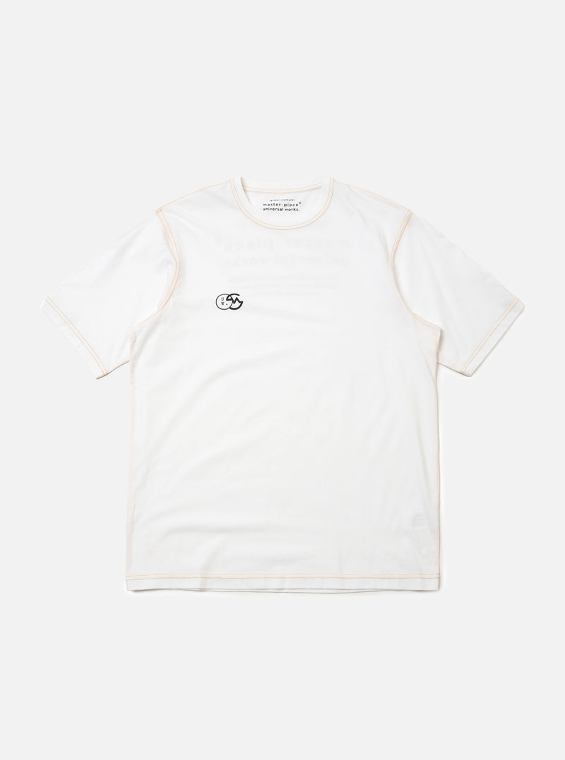 The master-piece x Universal Works White Single Jersey Print Tee is shown as a flat lay against a plain white background. This short-sleeved white t-shirt features a simple ribbed crew neckline and a relaxed fit. A small, dark graphic is printed on the left chest area, and a logo patch is visible near the front hem.