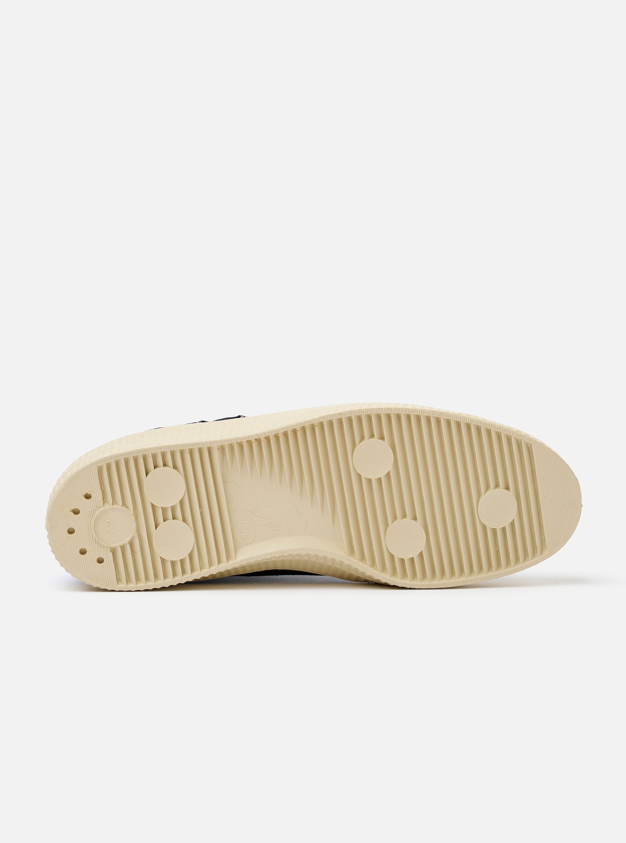 The Novesta for Universal Works Black/Pale Blue Canvas Star Master is shown from a side profile against a white background. The low-top sneaker features a black cotton canvas upper with contrast stitching, metallic eyelets, and a chunky ecru natural rubber sole with a textured tire-like finish on the toe cap. A prominent pale blue pull tab is located on the heel, and a dual-branded woven tag is visible on the tongue.