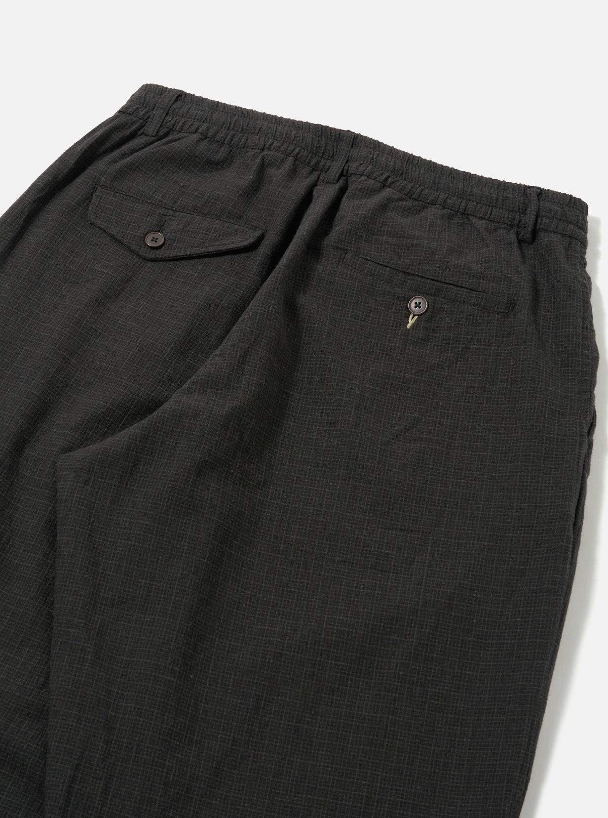 Close-up of the back of Charcoal Fine Linen Mix Pleated Track Pant on a white surface. Details include buttoned pockets and an elastic waistband.