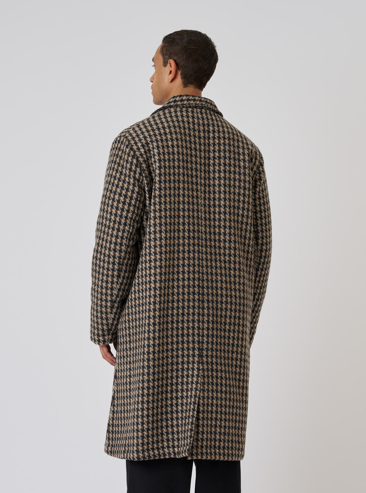 A man stands against a white backdrop, showcasing the back of a Sand Cortina Tweed Long Swing Coat. The coat features a tan and black tweed pattern.