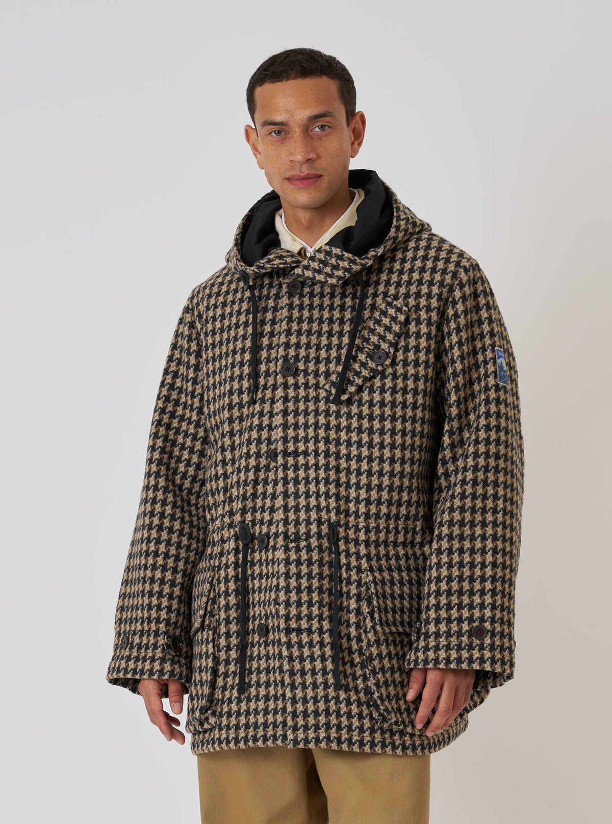 A model in a Sand Cortina Tweed Boston Parka. The parka is tweed with a black hood. The background is a plain white. The fit is relaxed and casual.