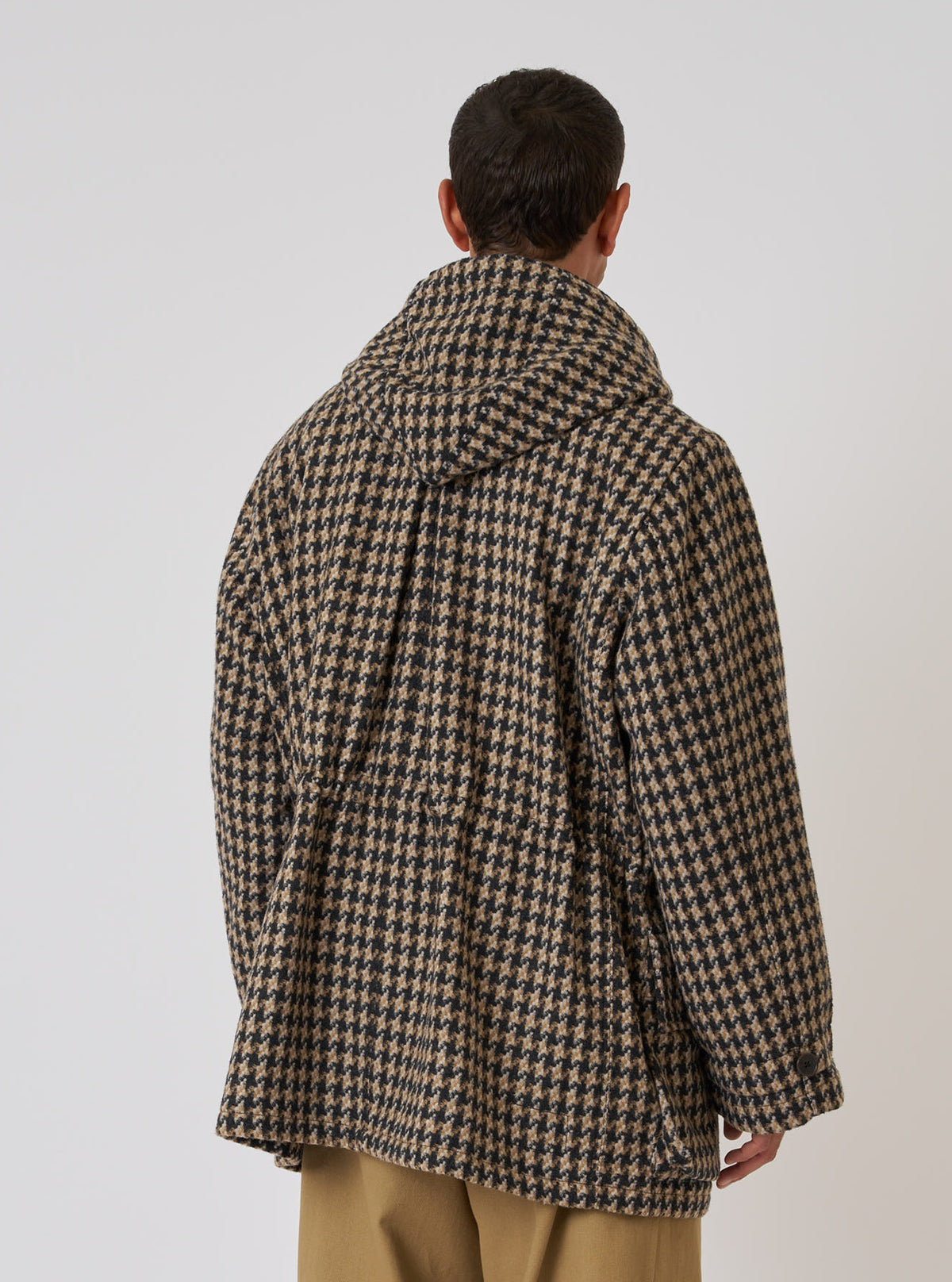 Back view of a model wearing the Sand Cortina Tweed Boston Parka. The parka is tweed with a black and tan houndstooth pattern. Shot against a white backdrop.