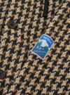 Close-up of the Sand Cortina Tweed Boston Parka showing the tweed fabric, buttons, and Hotel Deluxe patch. The background is a plain surface.