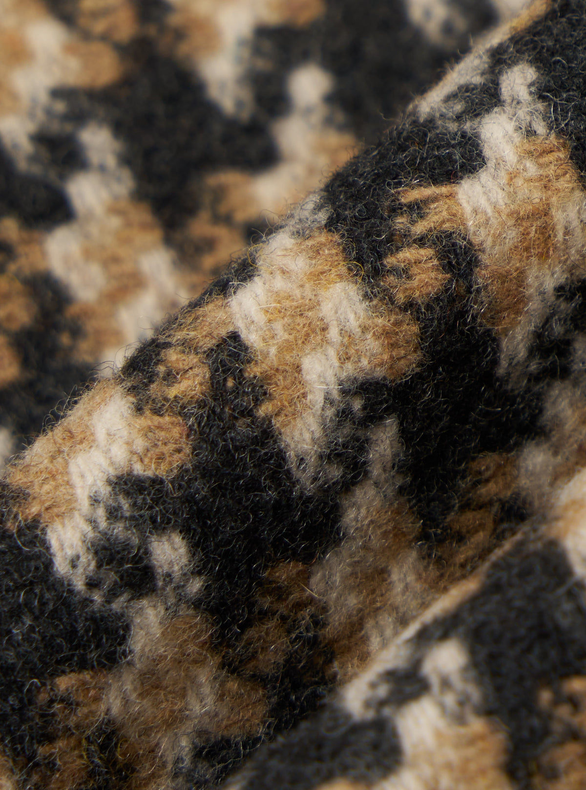 Close-up of the Sand Cortina Tweed Boston Parka fabric. The tweed has a textured feel with a mix of sand, black, and cream colors. The fabric is draped to show its texture.