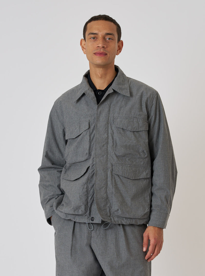 A model poses in front of a white background wearing a Charcoal Organic Chambray Parachute Field Jacket. The jacket is a light gray color and has four front pockets.