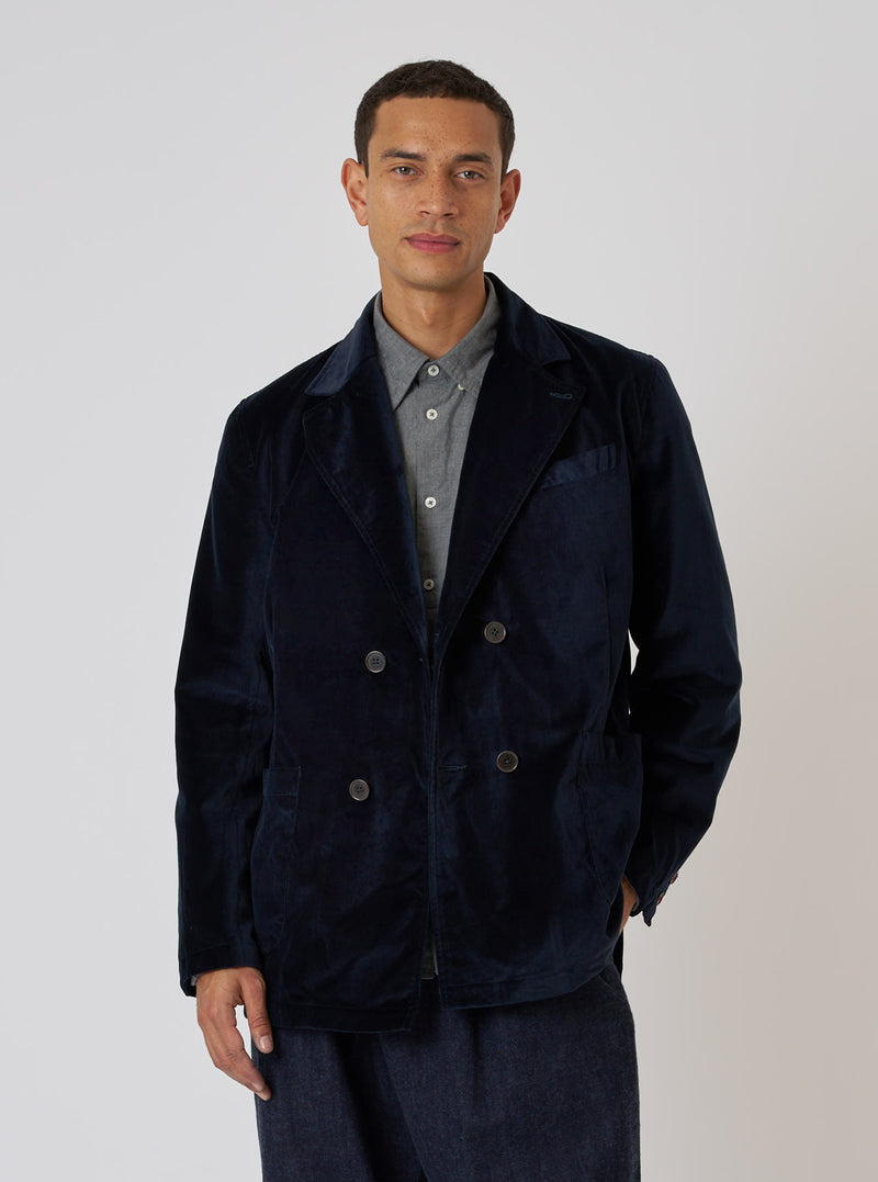 A model poses in front of a white backdrop, wearing the Navy Velveteen Manor Jacket. The jacket is a rich navy color and has a double-breasted fit.