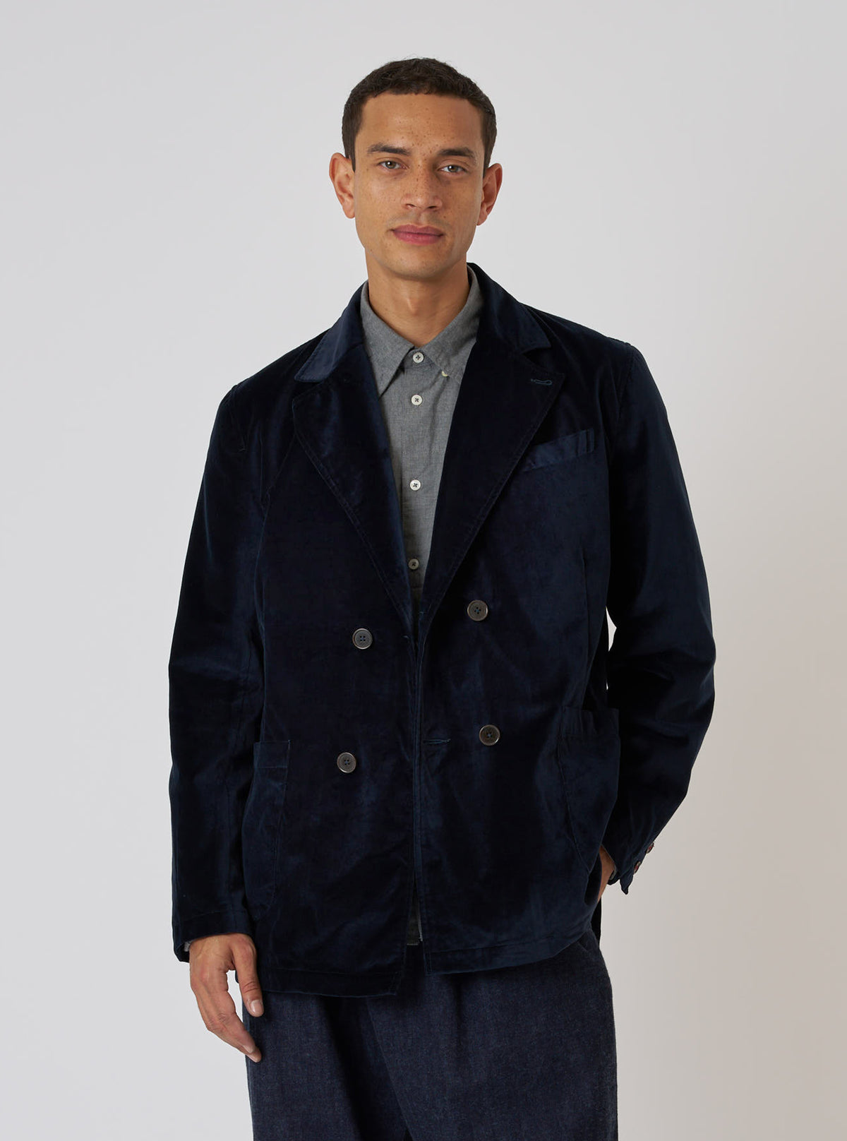 A model poses in front of a white backdrop, wearing the Navy Velveteen Manor Jacket. The jacket is a rich navy color and has a double-breasted fit.