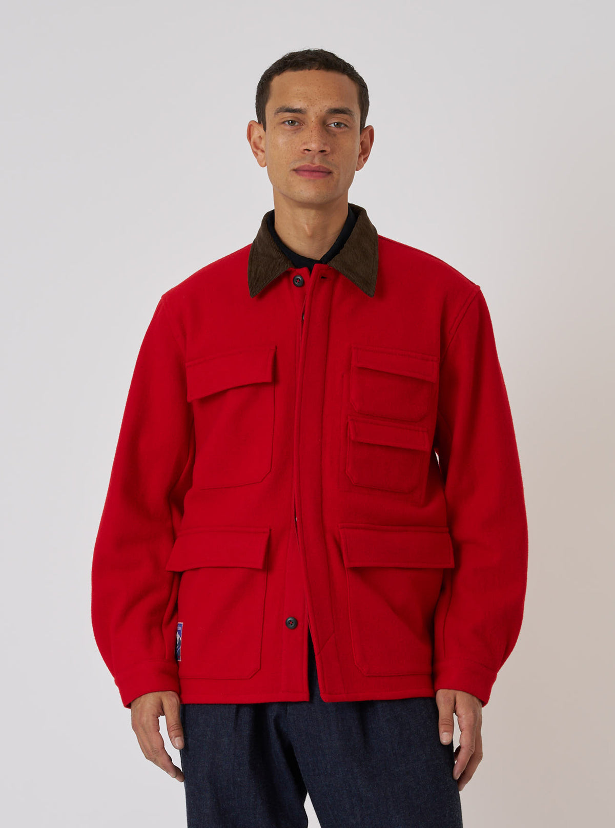 A model on a white background wears a Red Mowbray Military Fatigue Jacket. The jacket is wool with a corduroy collar and multiple pockets.