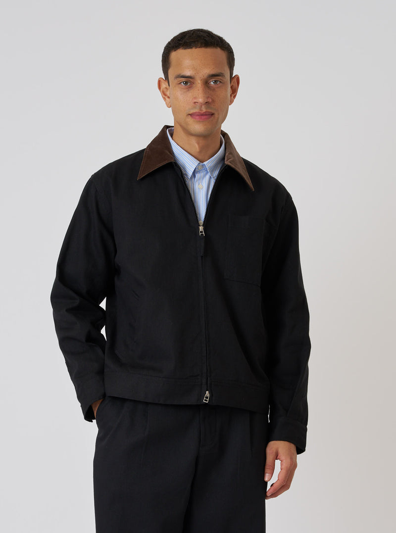 A model poses in a Black Works Twill Rose Bowl Jacket. The jacket is black twill with a brown corduroy collar. The background is a plain white studio backdrop.