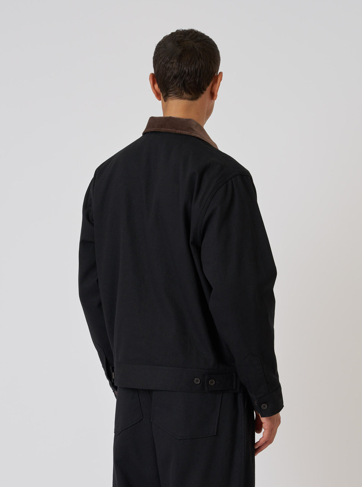 Back view of a model wearing the Black Works Twill Rose Bowl Jacket. The jacket is black twill with a brown corduroy collar. Shot against a white background.