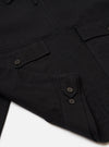 Close-up of the Black Organic Canvas S130 Jacket on a white surface. The jacket features a button-up design and visible pockets, showcasing its organic canvas material.