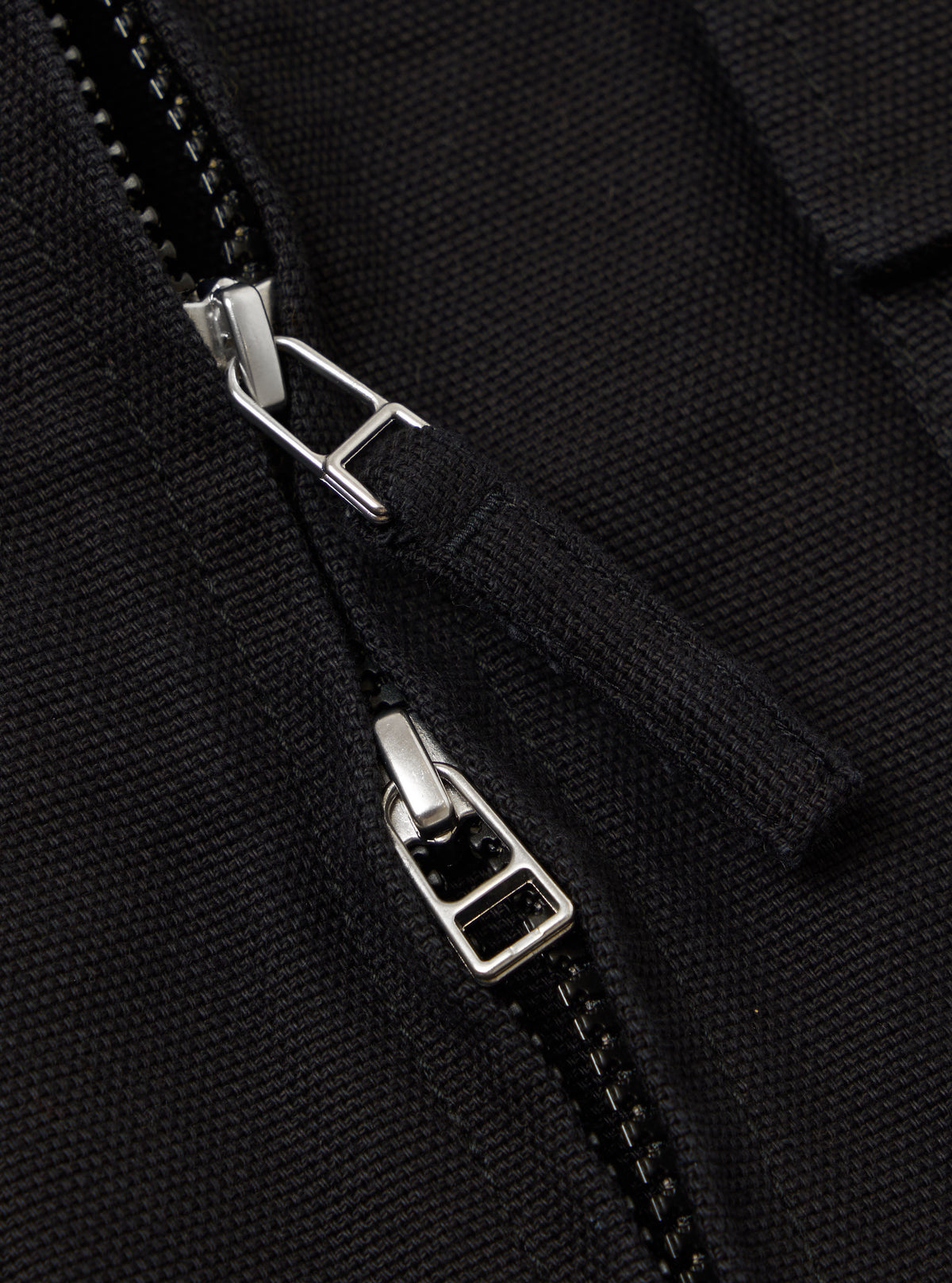 Close-up of the zipper on the Black Organic Canvas S130 Jacket. The black canvas material is visible, along with the silver zipper pull.