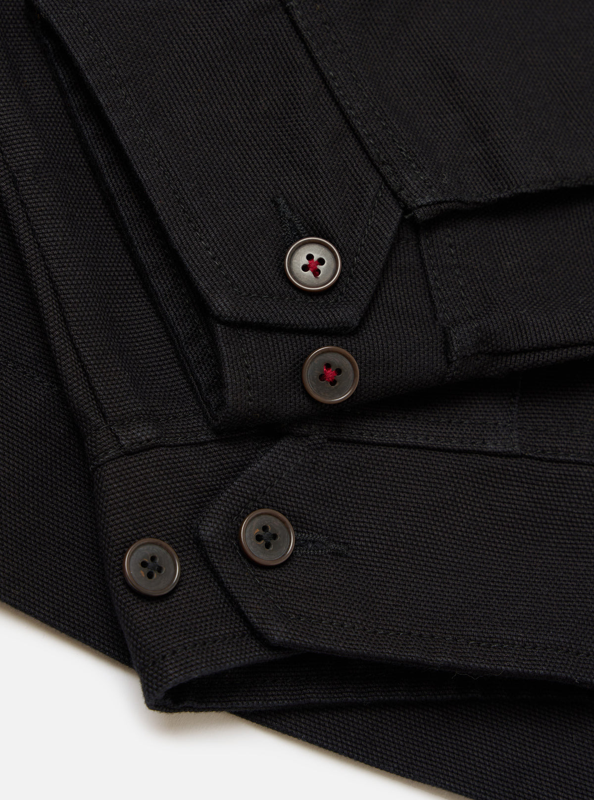 Close-up of the Black Organic Canvas S130 Jacket showing the black canvas material and buttons with red detail on a white background.