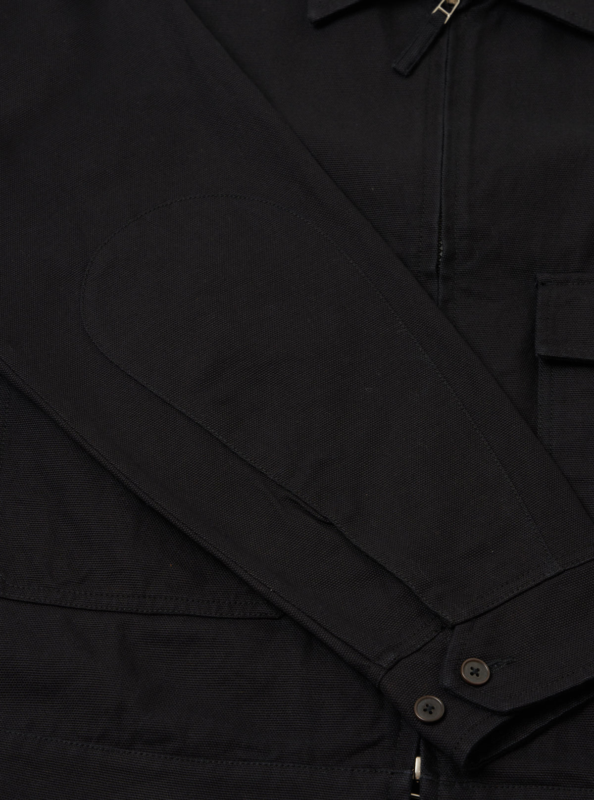 Close-up of the sleeve of a Black Organic Canvas S130 Jacket, showing the elbow patch, buttons, and canvas texture. Shot on a plain background.
