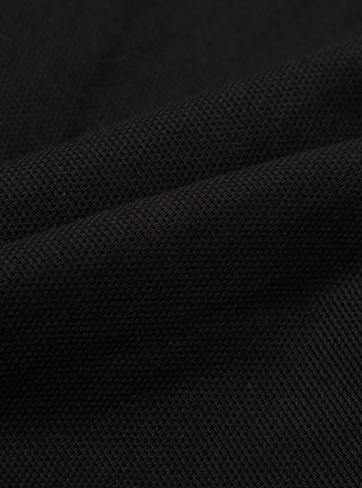Close-up of the Black Organic Canvas S130 Jacket, showcasing the texture and weave of the material. The fabric is draped to highlight its quality.