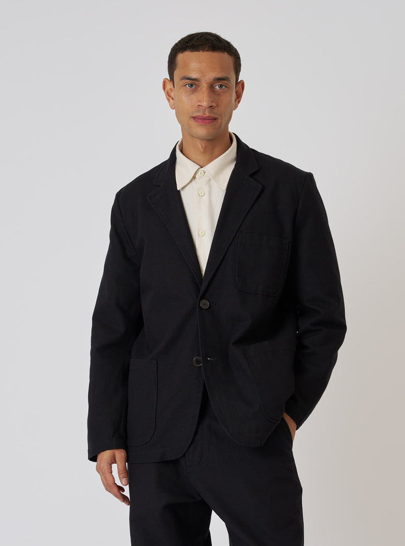 A model poses in a Black Organic Canvas Two Button Jacket against a white backdrop. The jacket is paired with a light-colored shirt for contrast.