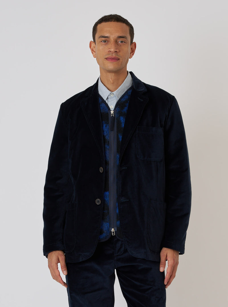 A model poses in front of a white background wearing a Navy Velveteen Two Button Jacket. The jacket is paired with a blue shirt and patterned vest.