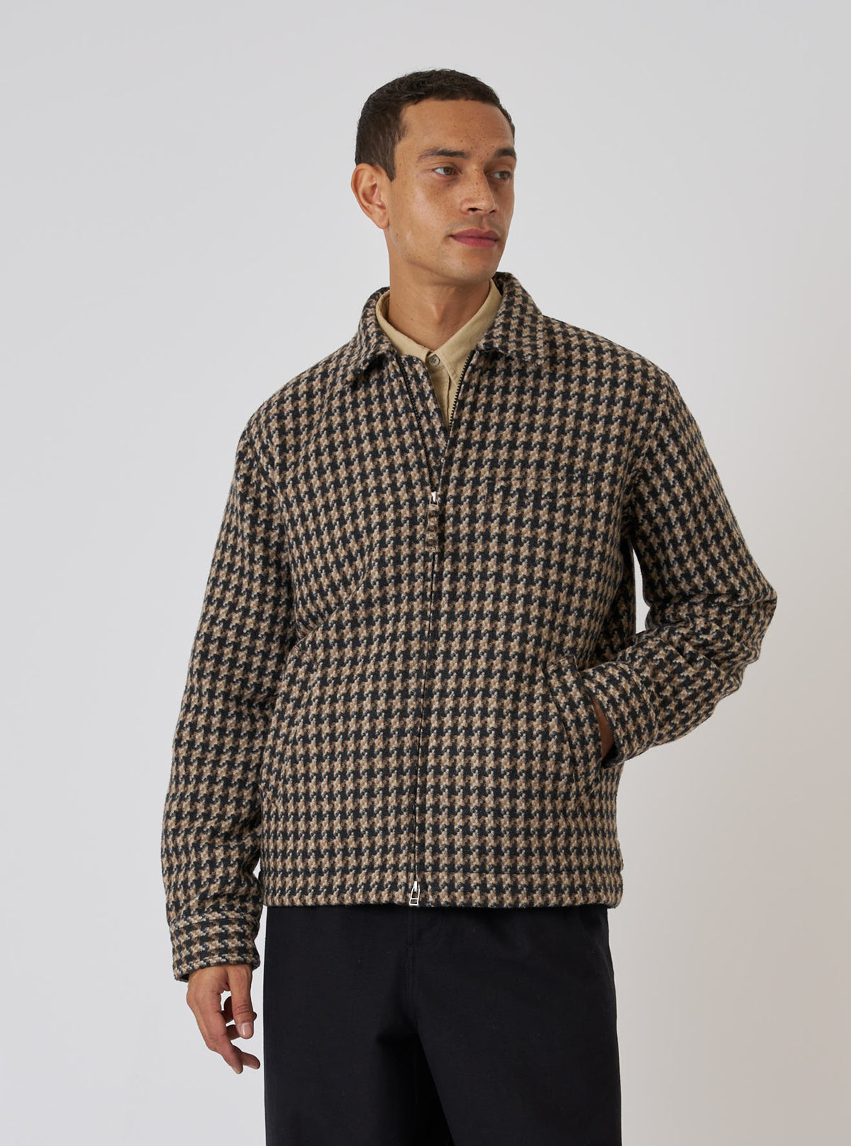 A model wears the Sand Cortina Tweed Windcheater, a brown and black tweed jacket, against a plain background. The jacket has a zip front and pockets.