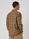 A man poses in front of a white background, wearing the Khaki Patch Check Twill Fatigue Shirt. The shirt is a khaki and brown plaid pattern. The model has his hands in his pockets.