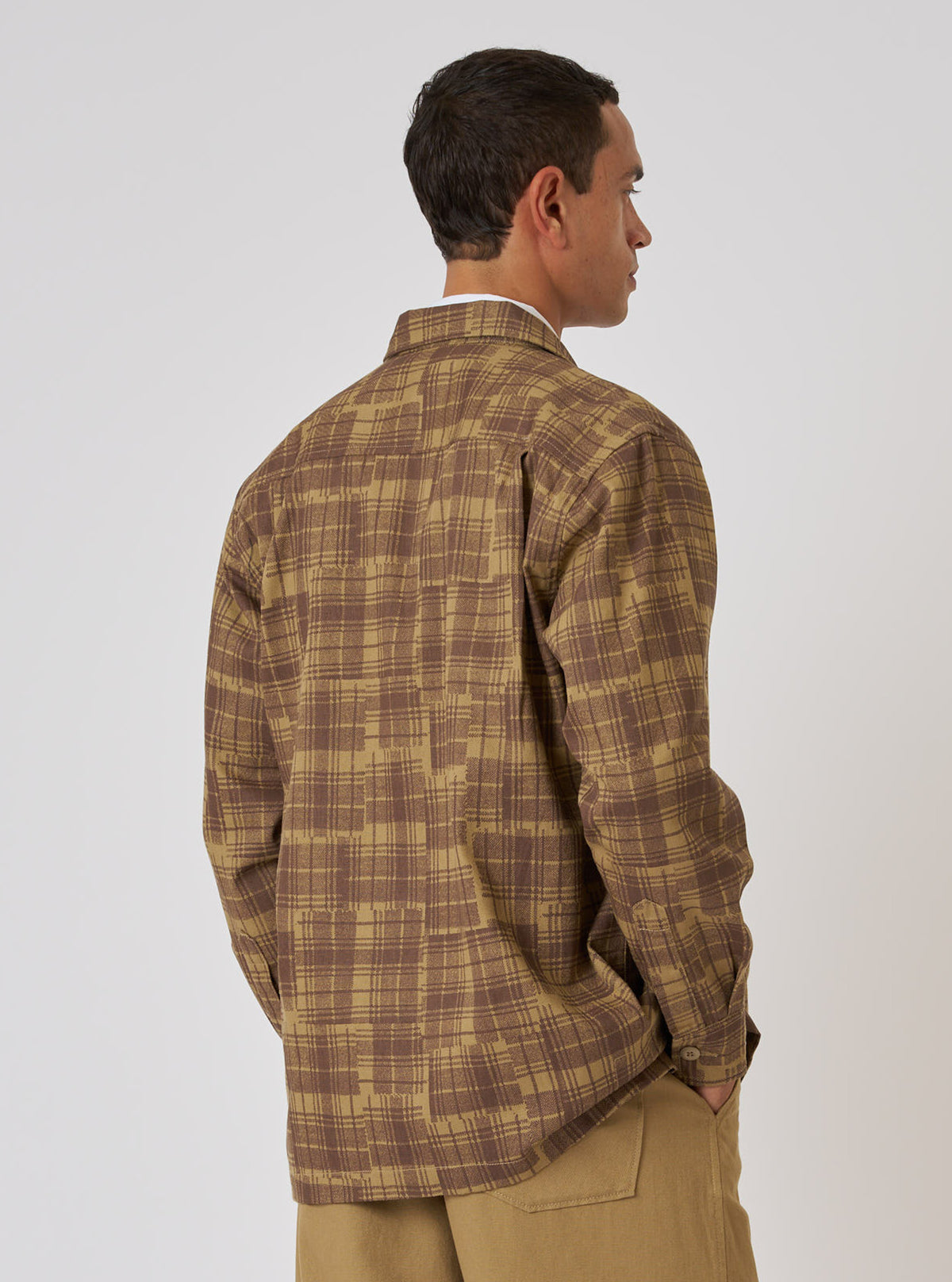 A man poses in front of a white background, wearing the Khaki Patch Check Twill Fatigue Shirt. The shirt is a khaki and brown plaid pattern. The model has his hands in his pockets.