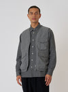 A model poses in front of a white background wearing a Charcoal Organic Chambray Parachute Liner Gilet. The gilet is charcoal gray and made of chambray material.